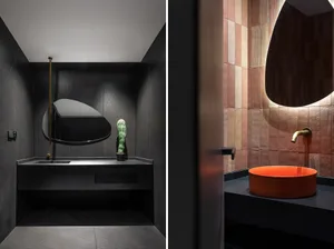 A modern bathroom with black metallic tiles, a unique mirror, and an orange sink.