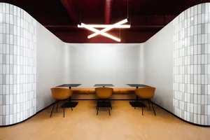 Modern industrial cafe interior with white tiled walls, cork flooring, and orange seating.