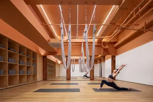 A woman practicing yoga in a minimalist fitness studio with hanging ropes.