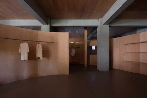 A modern clothing store with wood-paneled walls and floors, featuring minimalistic design elements and white garments hanging