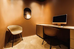 A modern minimalist workspace with a wooden counter, featuring two chairs and a desk with a computer setup.