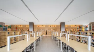 Minimalist design library with wood tables, glass shelves, and metal chairs.