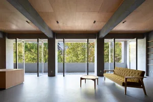 Modern living room with concrete and wooden elements, featuring large windows and a comfortable seating area.