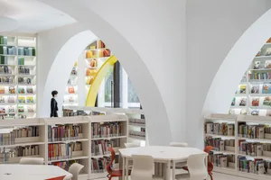 A modern library interior with white-painted walls, circular arches, and colorful bookshelves.