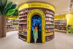 A children's library with an immersive room for ages 6-9, featuring wooden shelves filled with books and a digital screen wit