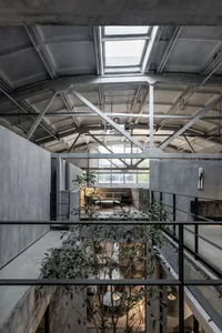 An industrial living room with concrete walls, large skylights, and potted plants.