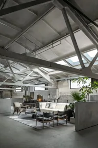 Industrial-style loft living space featuring exposed concrete beams, large windows, and minimalist furniture.