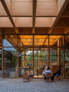 A modern, industrial-style restaurant interior with wooden structural beams and large glass windows.