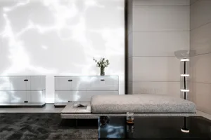 A minimalist living room features a glass matte table, a padded bench, and storage furniture in a sleek, modern design.