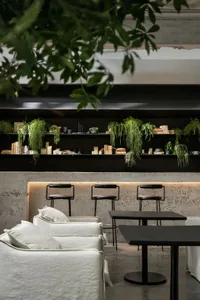 A modern cafe interior with concrete walls, metal furniture, and hanging plants.