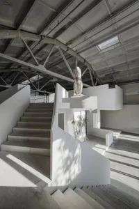 A minimalist interior space with exposed concrete walls, spiral staircase, and a white, modern sculpture.