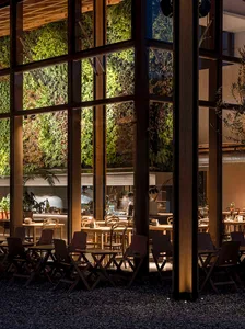 Industrial restaurant interior with wooden tables, chairs, and glass walls displaying greenery