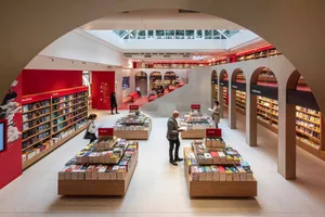 Modern bookstore interior with concrete columns, glass walls, and bookshelves filled with various books.