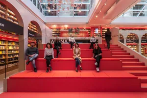 People sitting on red steps in a bookstore interior with a modern design.