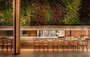 Modern restaurant interior featuring green vertical garden walls, wooden furniture, and a central bar counter.