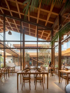 Interior of a modern cafe with wooden tables and chairs, large windows, and a spacious, airy atmosphere.