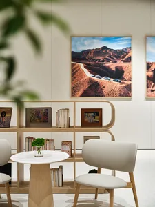 A modern library space featuring white marble tables, wooden chairs, and wooden shelves adorned with books, plants, and frame