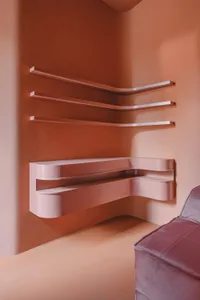 Modern minimalist metallic floating shelves mounted on a peach-colored wall.
