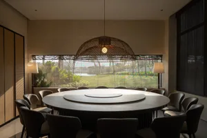 Modern dining room with a round wooden table and black chairs, featuring a large window with a view of a garden.