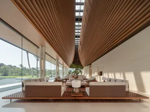 A modern lobby featuring elegant furniture, wooden panels, glass walls, and a large tree.