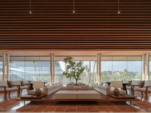 Modern resort lobby featuring wood and concrete materials, with seating arrangements and a central tree.