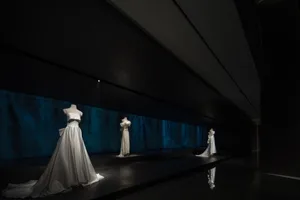 時尚展覽中，白色禮服整齊排列在模特兒身上，背景為深色戲劇性氛圍。