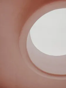 View of a minimalist architectural space with light-colored concrete walls and a circular opening allowing natural light to e