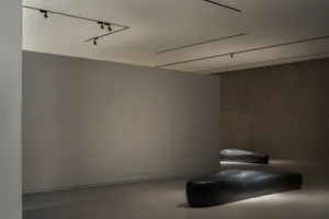 Minimalist modern interior space featuring smooth, textured concrete walls and floors, with contemporary seating and lighting