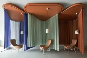 A modern living room with three wavy, curved textile dividers creating individual seating areas. Each divider is suspended fr