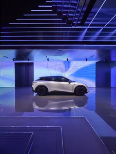 A sleek, white car displayed at a launch event with a futuristic interior and exterior design.