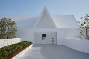A modern white building with glass features against a clear blue sky, with a child walking toward the entrance.