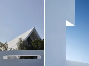 A minimalist building exterior with a white facade and a triangular roof.