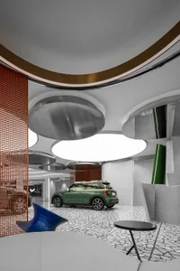 A modern car showroom with concrete flooring and metallic ceiling lighting, featuring a green car on display.