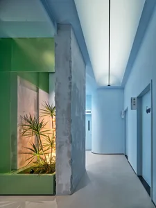 Modern interior corridor with concrete walls, green plant, and blue lighting.