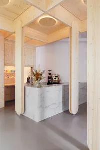 A modern minimalist coffee shop with a white marble and wooden countertop, featuring a minimalist coffee machine and a vase w