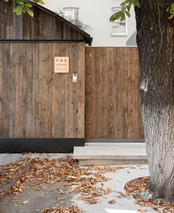 A wooden fence with a sign that reads 'TDC Clinic', surrounded by fallen leaves and a tree trunk.