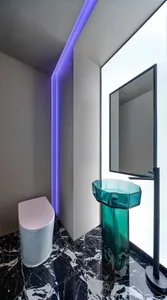 Modern bathroom featuring a transparent glass sink with purple LED lighting on the ceiling, and a black and white marble floo