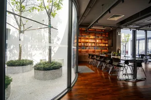 A modern library featuring wooden shelves and tables with large windows allowing natural light to enter.