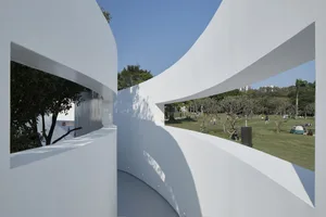 Curved concrete wall in a public outdoor space with people and trees in the background.