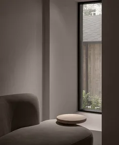 Modern minimalist living room with a grey sofa, wooden coffee table, and a tall window showcasing a garden.
