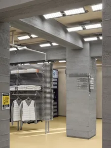 Concrete retail shop interior with clothing racks and signage.