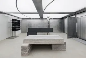 A minimalist industrial-style lobby featuring a large concrete table and a wall-mounted speaker system.