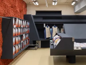 Industrial-style clothing store interior with concrete walls, metal shelves, and glass display cases.