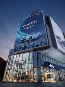 A large glass-fronted building with a large Jeep advertisement at night.