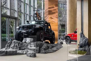 A modern retail shop with a concrete interior design, featuring a jeep on a rocky platform and a sand dune mural in the backg