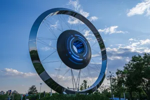 A large circular metal sculpture with a glowing blue center, set against a blue sky with clouds.