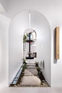 A minimalist showroom interior with concrete flooring, a plant-lined walkway, and a display area.