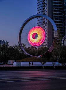 A modern metallic sculpture with a glowing center, located in an urban setting.