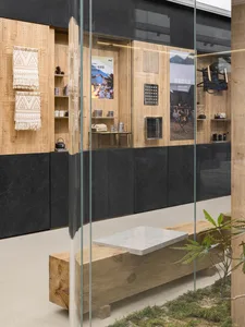 Modern retail storefront with wooden shelves, glass display cases, and a cozy seating area with cushioned stools and a plant.