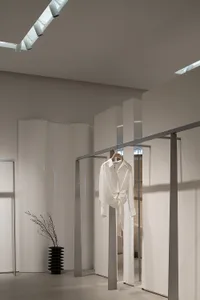 Modern minimalist clothing store interior with white walls, glass panels, and a single white blouse hanging on a rail.